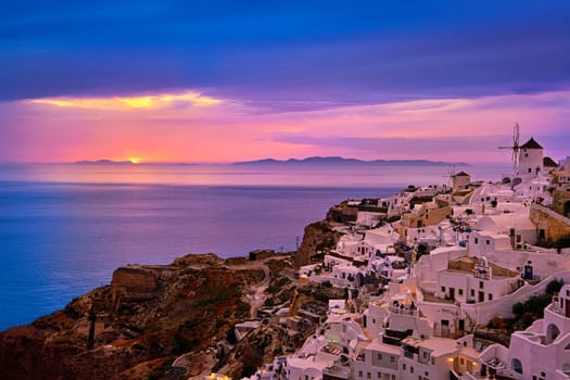 Beautiful view of Oia village with traditional whitewashed houses and windmills, Santorini island, at sunset, Greece. Scenic travel background, famous destination, colorful sky and clouds.