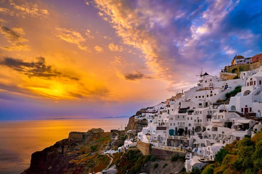 Beautiful view of Oia village with traditional whitewashed houses and windmills, Santorini island, at sunset, Greece. Scenic travel background, famous destination, colorful sky and clouds.