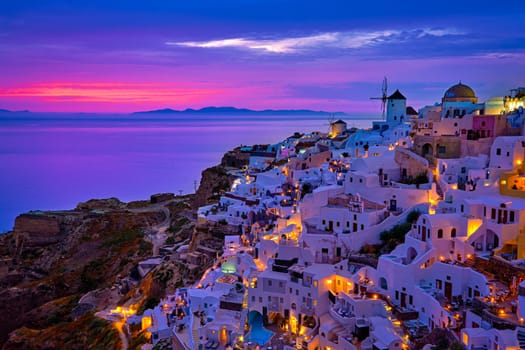 Beautiful view of Oia village with traditional whitewashed houses and windmills, Santorini island, at sunset, Greece. Scenic travel background, famous destination, colorful sky and clouds.