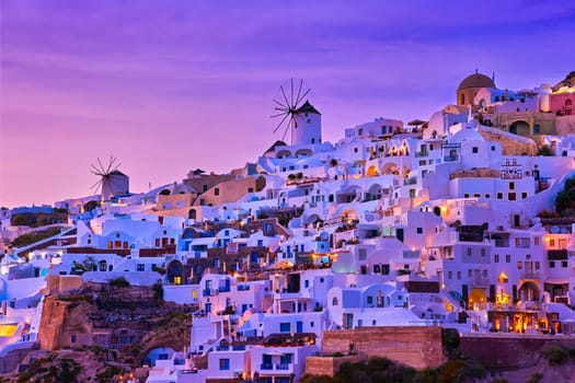 Beautiful view of Oia village with traditional whitewashed houses and windmills, Santorini island, at sunset, Greece. Scenic travel background, famous destination, colorful sky and clouds.