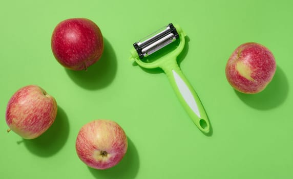 Red apples and peeler on green background, top view