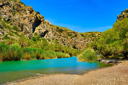 View of Kourtaliotis river and canyon near Preveli beach at Libyan sea, river and palm forest, southern Crete, Greece on clear sunny day. Travel destinations, gorge, blue sky with clouds, summer, sunshine, hiking, vacations, Mediterranean sea.