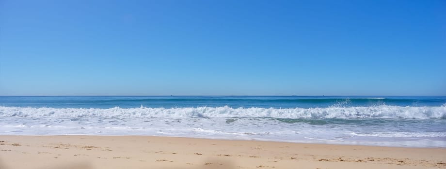 Blue sky, breaking surf waves and sandy beach on a calm sunny day on the water's edge as the tide comes in along the shoreline of Kawana Beach, Sunshine Coast, Queensland, Australia