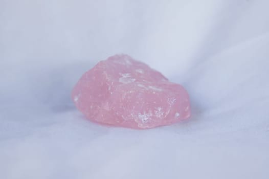 Rose quartz fragment, believed to have beneficial health properties. Isolated over white fabric cloth