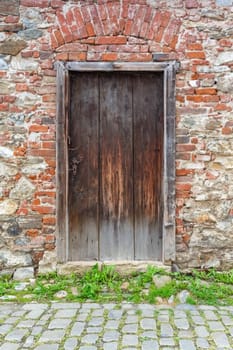 Old rustic wooden door in brick and stone wall background. Vertically.