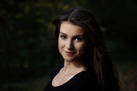 Portrait of attractive long haired young woman posing outdoors on dark background.  Horizontally.