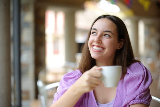 Happy woman dreaming looking above drinking coffee in a restaurant