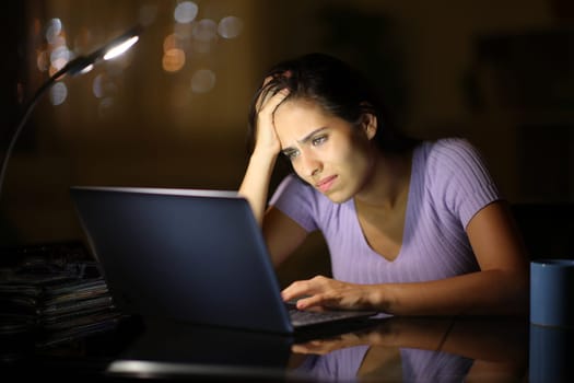 Sad woman complaining in the night at home cheking bad news on laptop