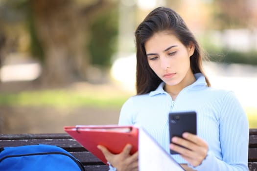 Student checking smart phone sitting in a park