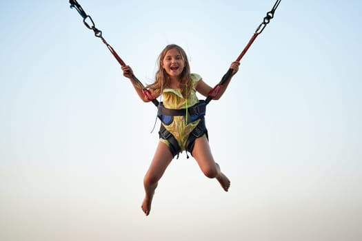 Bungee jumping at trampoline. Little girl bouncing on bungee jumping in amusement park on summer vacations. Kid flying over blue sky while jumping on trampoline