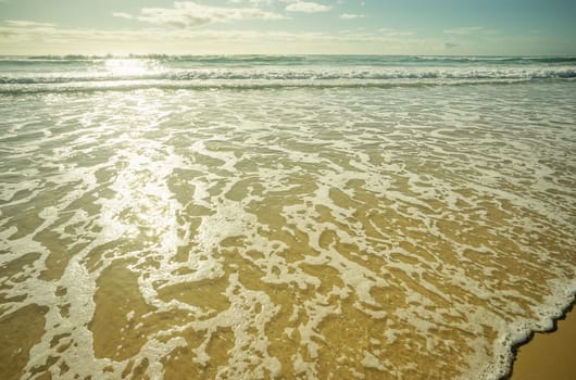 Foamy white wash as waves break and roll across the sandy beach. Empty background concept with copy space for seaside holiday, vacation, honeymoon, relaxation, inspiration, meditation, relaxing