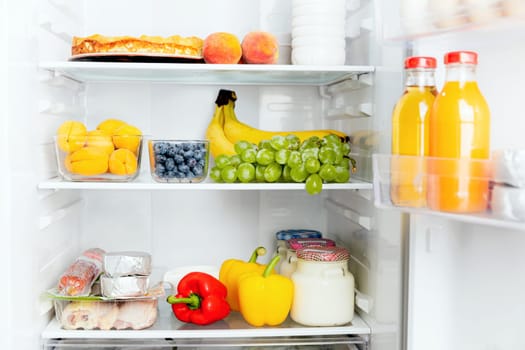 Front View of open two door fridge or refrigerator door filled with fresh fruits, vegetables, juice, full of healthy food items and ingredients inside. Electric Kitchen and Domestic Major Appliances