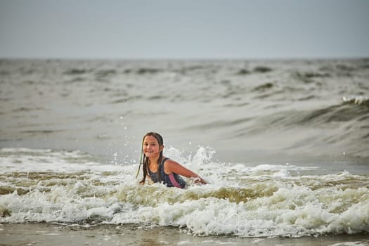 Little girl playing with waves in the sea. Kid playfully splashing in waves. Child jumping in sea. Vacations on the beach. Water splashes. Fun and play during summer vacation. Travel concept