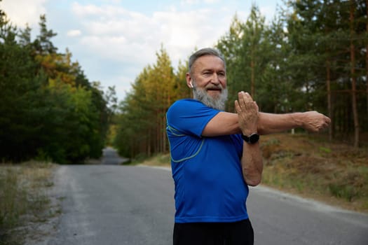 Happy retired sportsman stretching arms before running race start. Warm up workout and cardio exercise preparation