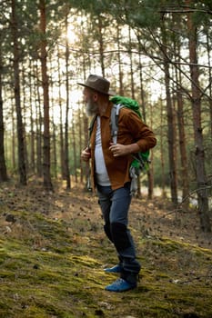 Retired man with backpack walking touristic footpath in forest. Authentic male tourist lifestyle on retirement