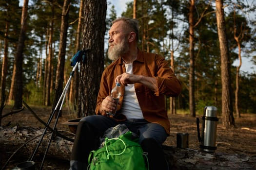 Senior male hiker or wilderness explorer taking break during hiking in pine forest. Expedition enjoyment on retirement