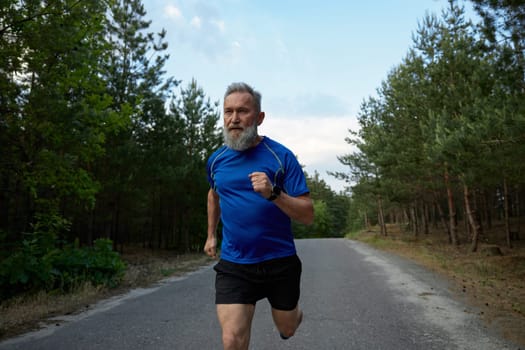 Senior sportsman running among countryside road. Physical endurance training and cardio exercise for pensioner