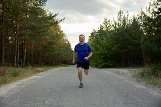 Senior man running outside among countryside road. Healthy lifestyle and physical activity for wellness on retirement