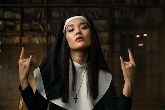 Portrait of passionate catholic nun gesturing heavy metal rock symbol with two hands. Rock-and-roll music, religion and desire concept