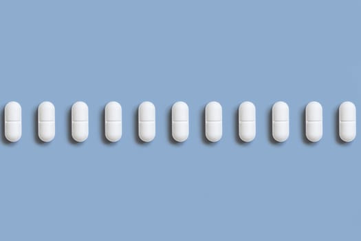 Mix of white medical pills in a line on light blue top view. Preventive medicine and healthcare, dietary supplements and vitamins. Assorted pharmaceutical medicine capsules
