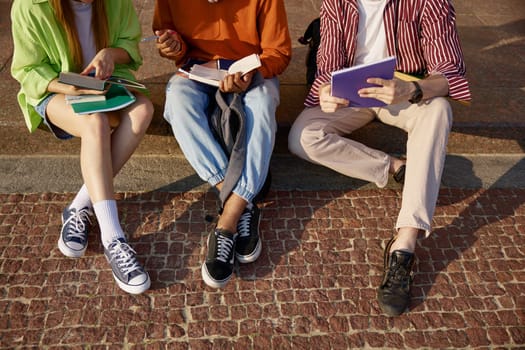 Closeup cropped shot of male and female students group doing homework outdoors. Classmates preparing for exam or creating school project together at campus park