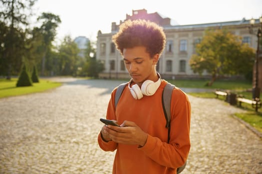 Teenager boy student using mobile phone standing outdoors. Break time at high school, university or college