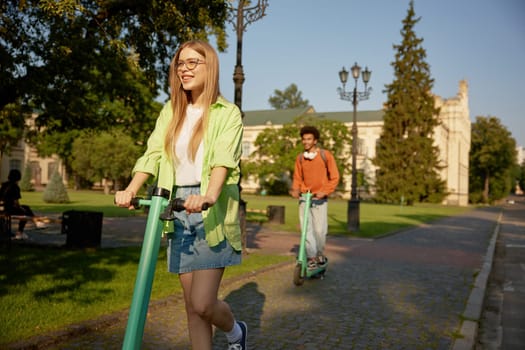 Company of students using electric scooter vehicles riding among university campus pathway