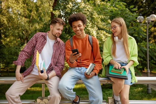 Confident smiling university students chatting together while taking rest at outdoor campus park. Nice conversation of international millennial people group