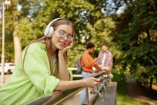 Dreamy teenage female student in headphones relaxing listening music and enjoying free time after university lessons