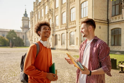 Happy positive male students talking together after classes. Millennial guys sharing expression while having meeting at university campus
