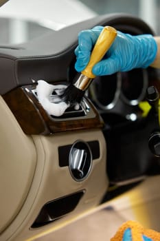 Car detailing, procedure. Closeup master washing dashboard using soft brush and special auto cosmetics for plastic parts cleansing from dust and dirt