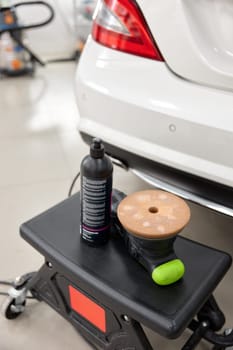 Bottle of special wax or polish cream and disk grinding machine for car paint coating refreshment. Auto detailing and polishing service
