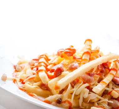 Closeup of french fries served in restaurant plate isolated on white background. Fried potato with ketchup, cheese and bacon. Fast food restaurant menu.