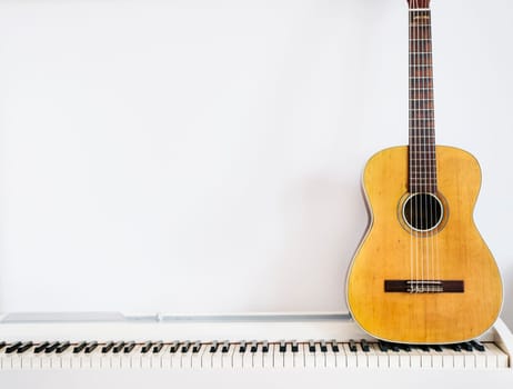Acoustic guitar on piano keyboard in front of white wall. Music instrument background.