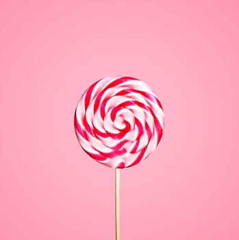 Colorful red and white lollipop candy on pastel pink background. Sweet sugar candy swirl in modern fashion style. Minimal flat lay design. Food fun for kids concept.