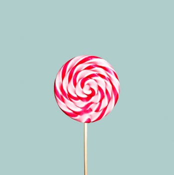 Colorful pink and white lollipop on pastel vintage blue background. Sweet sugar candy swirl in modern fashion style. Minimal flat lay design. Food fun for kids concept.