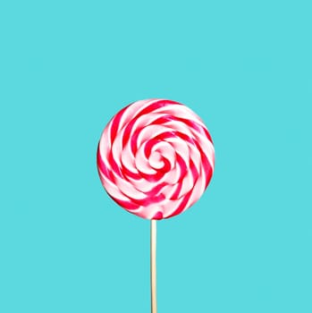 Colorful red and pink lollipop on pastel blue background. Sweet sugar candy swirl in modern fashion style. Minimal flat lay design. Food fun for kids concept.