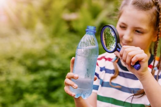 Girl studying water in a bottle with a magnifying glass. Concept of the pure water.