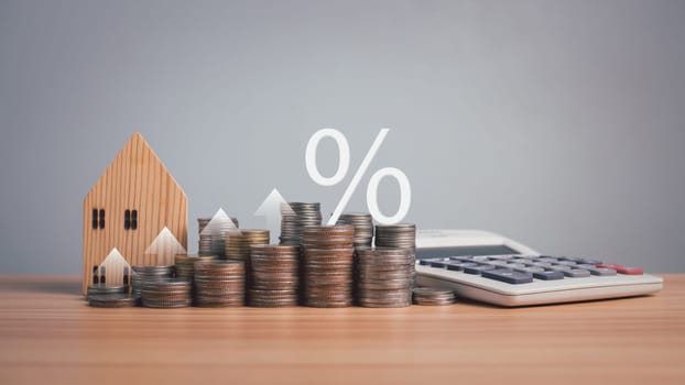 Model wooden house, calculator and coins lined up on wooden floor on white background. Concepts of mortgage, loand, transfer, finance, savings and investment. Real estate tax concepts.