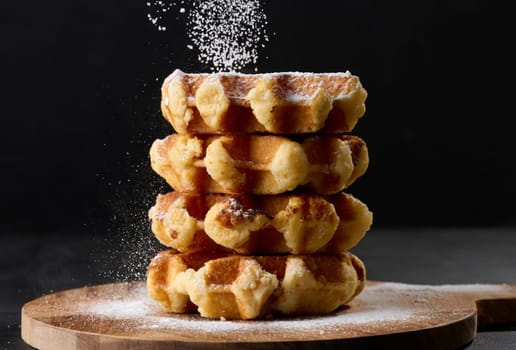 A stack of baked Belgian waffles sprinkled with powdered sugar