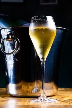 Bottle and cup of champagne on a wooden table, dark background