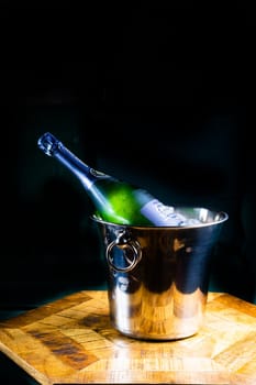 Bottle and cup of champagne on a wooden table, dark background