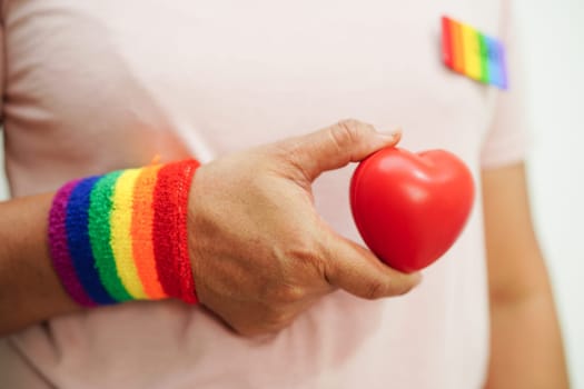 Asian woman holding red heart with rainbow flag, LGBT symbol rights and gender equality, LGBT Pride Month in June.