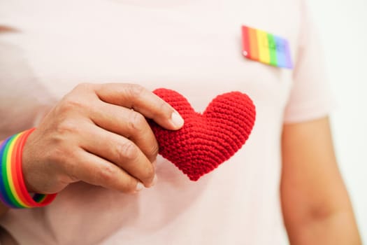 Asian woman holding red heart with rainbow flag, LGBT symbol rights and gender equality, LGBT Pride Month in June.