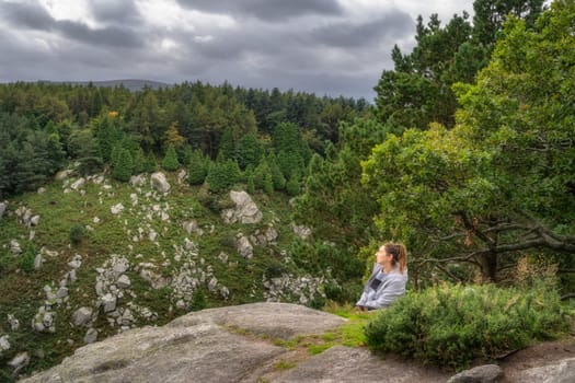 Adult woman leaning over a rock in Lead Mines, with a beautiful view on a valley and forest in background. Hiking in Wicklow Mountains, Ireland