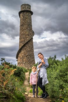 Mother and daughter standing in front of old and abandoned stone chimney with external spiral stairs in Lead Mines, Wicklow Mountains, Ireland