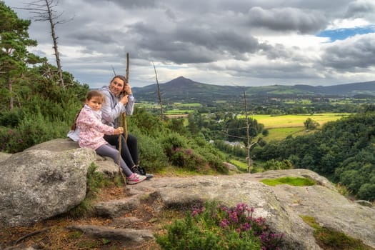 Mother and daughter standing on a rock in Lead mines, with a scenic view on a valley and pine forest. Family hike in Wicklow Mountains, Ireland