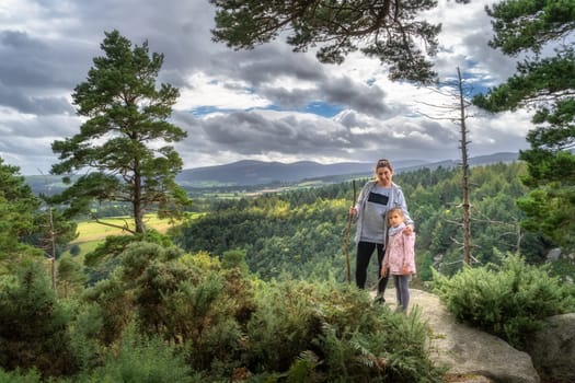 Mother and daughter standing on the edge of cliff in Lead mines, with a view on a valley and pine forest. Family hike in Wicklow Mountains, Ireland