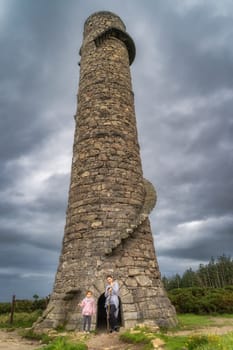 Mother and daughter standing at the entrance to old and abandoned stone chimney with external spiral stairs in Lead Mines, Wicklow Mountains, Ireland