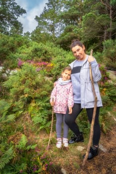 Mother and daughter standing on hill, surrounded by colourful heathers, ferns and pine forest. Family hike in Lead Mines, Wicklow Mountains, Ireland